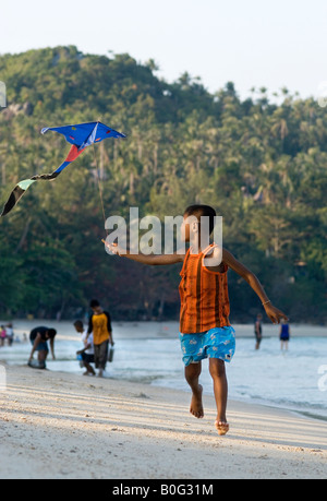 A Thai boy attempts to launch his bat kite on the beach of his tropical island home Stock Photo
