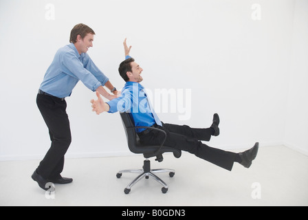 Man pushes man in office chair Stock Photo