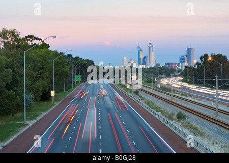 Busy traffic at dusk on the Mitchell Freeway heading towards Perth, Western Australia. Perth's skyscrapers are in the distance. Stock Photo