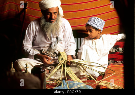A man teaching a child how to weave a basket, Oman.