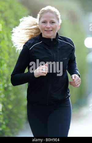 Young, smiling blonde woman wearing black tracksuit jogging Stock Photo