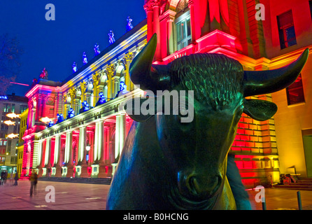 The bull of the Bull and Bear in front of the brightly lit Frankfurt Stock Exchange at night, illuminated by multicoloured spot Stock Photo