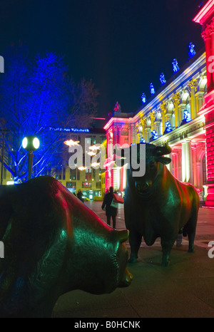 The Bull and Bear statue in front of the brightly lit Frankfurt Stock Exchange at night, illuminated by multicoloured spotlight Stock Photo