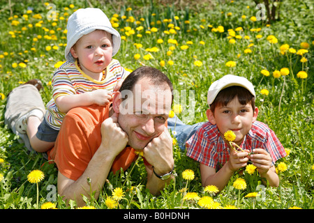 Father, Gaudenz Huggel, and his two sons lying on a dandelion meadow, Arlesheim, Baselland, Switzerland Stock Photo