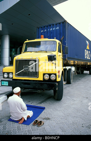 A Muslim driver kneeling to pray in front of his truck, United Arab Emirates. Stock Photo