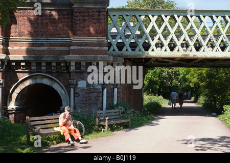 A Young Man sits smoking his Bike leant up against a bench by Kew Railway Bridge on the Thames Path Stock Photo