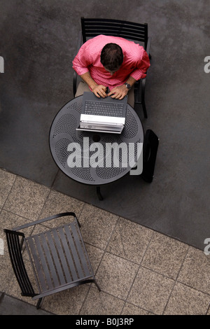 Aerial view of a young man sitting at an outdoor cafe, working on his laptop computer. Stock Photo