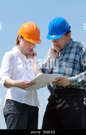 Young couple wearing helmets studying building plans of their new house Stock Photo