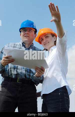 Young couple wearing helmets visualizing their new future house based on their building project documentation Stock Photo