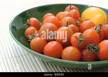 Orange cherry tomatoes and one yellow tomato in a green bowl Stock Photo