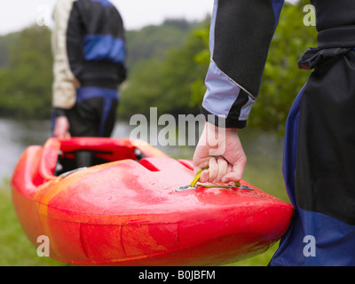 Two men carrying kayak to river Stock Photo