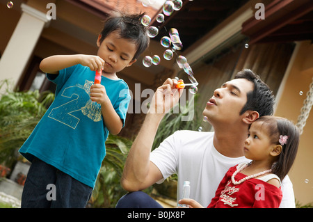 Father having fun with his two children, blowing soap bubbles together Stock Photo