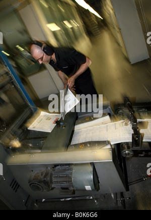 A worker checks copies of newspapers as they are printed on printing presses at Newsfax in East London U K Stock Photo