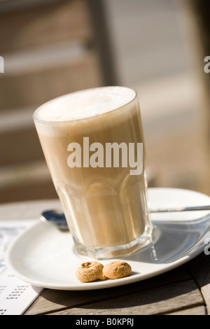 glass of Latte Macchiato outside on italian street café table, on plate, with amarettini Stock Photo