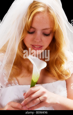 Beautiful blond haired woman glows in her bridal veil and dress as she smells a lily Stock Photo