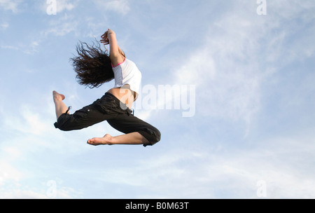 A young woman flying high on a trampoline against the sky, UK Stock Photo