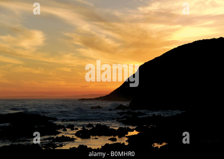 An array of beautiful colours fills the sky as the evening sun dips behind the headland at Tsitsikama National Park. Stock Photo