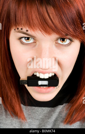 Beautiful redhead girl biting an usb memory stick with eyes on fire Concept alluding to hate against computers Stock Photo