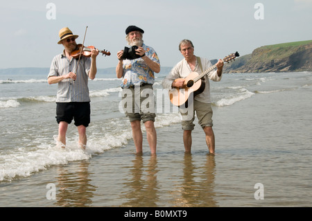Three traditional acoustic folk musicians playing music on the beach and paddling in the sea at Druidston Haven Pembrokeshire UK Stock Photo