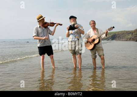 Three traditional acoustic folk musicians playing music on the beach and paddling in the sea at Druidston Haven Pembrokeshire UK Stock Photo