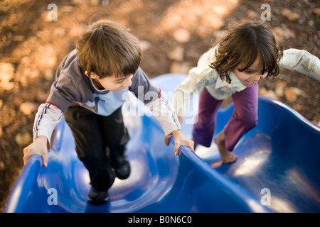 Six year old boy challenges his four year old sister to a race up the slide. Barefoot and confident she overtook him and won Stock Photo