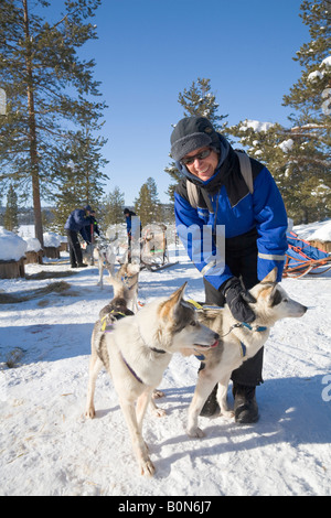 A woman strokes a husky at a dogsledge ride with siberian huskies in winterly Lapland / northern Sweden