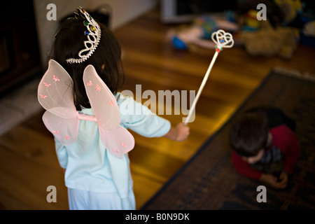 Four year old girl in fairy costume casts a spell on her six year old brother kneeling in the shadows
