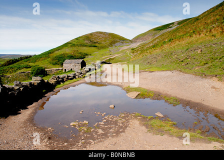 Site of old lead mine workings with stone barn in background and water in foreground Swaledale Yorkshire Dales England UK Stock Photo