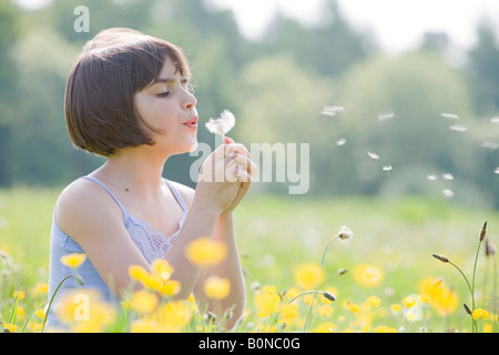 young female child sitting in field of buttercups blowing a dandelion with room for copy Stock Photo