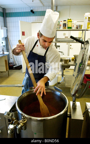 A cook stiring a large pot in a restaurant kitchen in Sweden Stock Photo