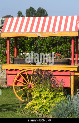 Covered Garden Cart With Red and White Striped Awning and Two Large Wheels Used to Hold Bedding Plants West Sussex England UK Stock Photo