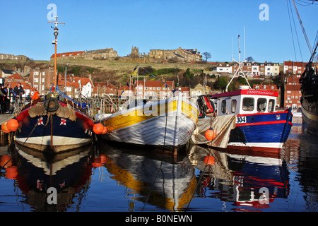 Working fishing boats in Whitby Harbour, with abbey behind and against a blue sky. Stock Photo