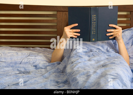 A woman reading a book in bed Stock Photo