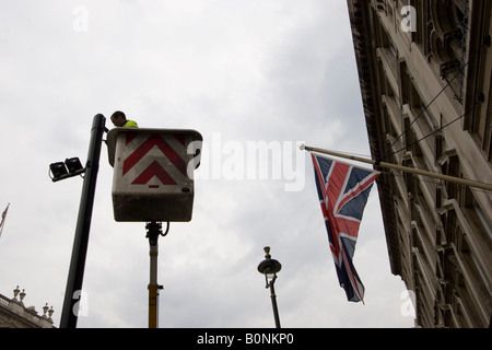 workman in cherry picker maintaining cctv close circuit television cameras, Whitehall London UK with Union Jack, Union Flag in background Stock Photo