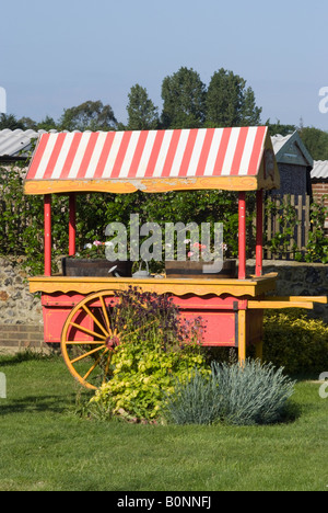 Covered Garden Cart With Red and White Striped Awning and Two Large Wheels Used to Hold Bedding Plants West Sussex England UK Stock Photo