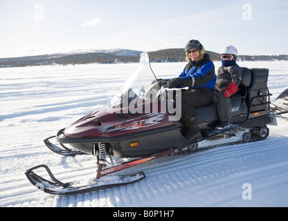 A woman in her fourties rides a Lynx snowmobile in snowy Lapland, a six years old girl is sitting on the back seat Stock Photo
