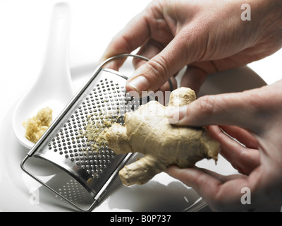 person grating root ginger stem on grater Stock Photo