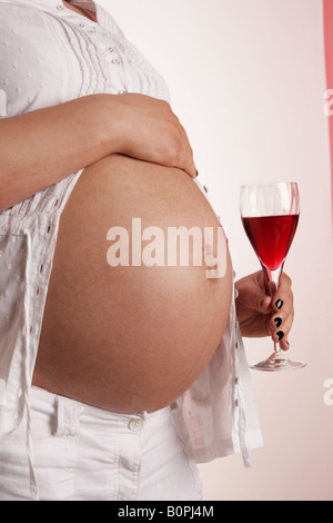 pregnant woman holding red wine in glass next to her exposed bear stomach . Stock Photo