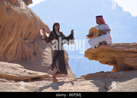 Jordan. Desert Wadi Ram. The young woman in national clothes dances. Young man plays on a musical instrument. Stock Photo