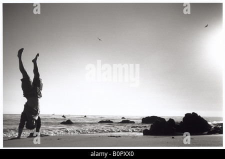 silhouette of man on beach doing handstand black and white horizontal Stock Photo