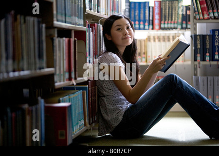 Young woman sitting on floor in library holding book Stock Photo