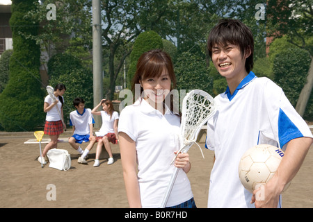 Portrait of teenage couple holding sports equipment with friends in background Stock Photo