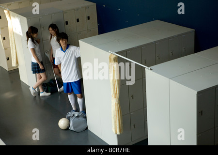 Two teenage girls and teenage boys standing by lockers in hallway Stock Photo