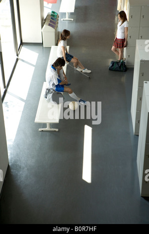 Two teenage girls and teenage boys standing by lockers in hallway Stock Photo