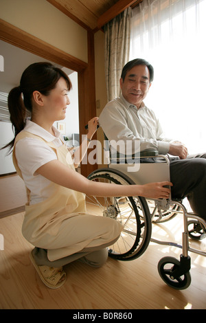 Female nurse crouching next to elderly man sitting in wheelchair Stock Photo