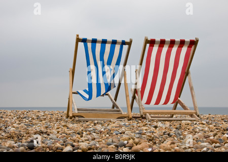 Red and blue deckchair lie empty on a british beach on a windy day out of season in the summer holidays Stock Photo