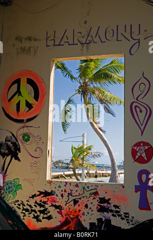 Palm trees and blue sky on a windy day as seen through a window with symbols and paintings on the walls, Caye Caulker , Belize Stock Photo