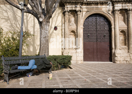 Drunk homeless sleeping on a bench in front of a Renaissance facade, Seville, Spain Stock Photo
