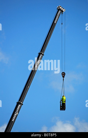two construction workers being lowered on to the roof of building by a high rise crane Stock Photo