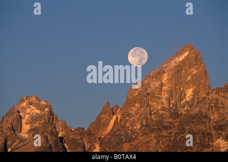 Full moon setting over the summit of the Grand Teton mountain at sunrise Grand Teton National Park Wyoming Stock Photo